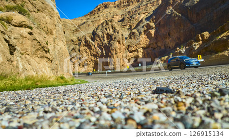Blue SUV in Motion on Winding Desert Canyon Road with Steep Rock Walls Low Angle 126915134