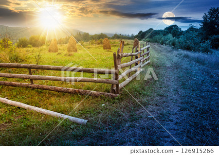 rural field behind the wooden fence. day and night time change concept. countryside landscape in mountains with sun and moon at twilight. organic haystack on the meadow rural field behind the wooden fence. day and night time change concept. countryside landscape in mountains with sun and moon at twilight. organic haystack on the meadow 126915266