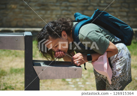 Young Woman Refreshing Herself at an Outdoor Drinking Fountain on a Sunny Day 126915364