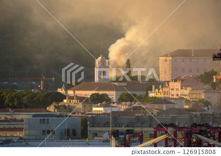 Lisbon church tower in sundown light surrounded by historic buildings and column of rising smoke in air. Soft sunlight, city architecture, beautiful tranquil urban skyline, risk of fires, damage 126915808