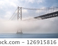 Iconic 25 de Abril suspension bridge, Lisbon, Portugal, in morning fog on sunny day over calm Tagus river waters. Misty atmosphere, peaceful, quiet scene, mist roll in over waters, riverscape, beauty 126915816