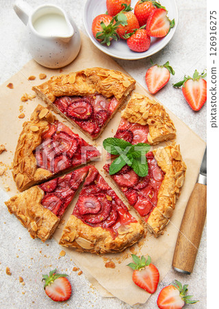 Delicious homemade strawberry galette with almond flakes being sliced on baking paper 126916275