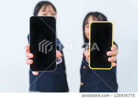Two girls in uniforms showing their smartphone screens Two girls in uniforms showing their smartphone screens 126916778