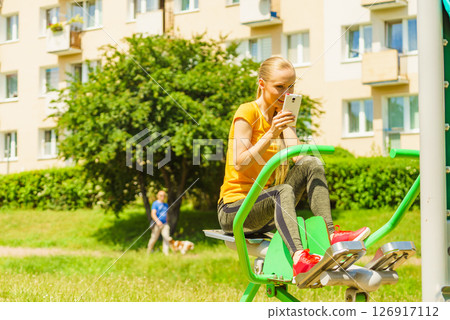 Girl doing exercises outdoor, holding phone Girl doing exercises outdoor, holding phone 126917112
