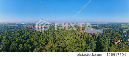 Panoramic aerial view of lush green forest and small European town with red roofs under clear blue sky. Rural landscape Panoramic aerial view of lush green forest and small European town with red roofs under clear blue sky. Rural landscape 126917304