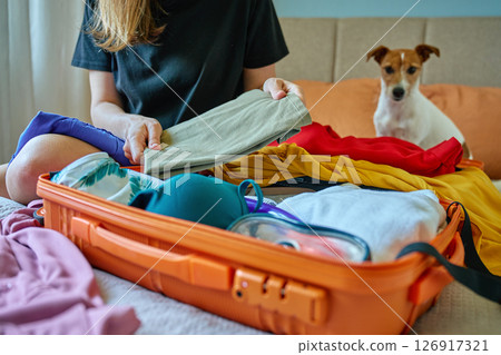 Woman preparing for vacation, packing bright orange suitcase with swimwear and summer clothes on bed. Vacation preparation 126917321