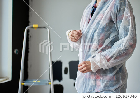 Close-up of woman in protective coveralls preparing to paint wall with color samples in new apartment. Concept of home improvement, renovation and interior updates 126917340