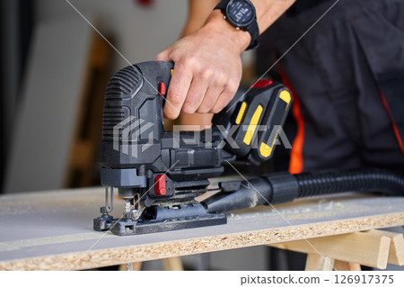 Close up of electrical handheld jigsaw cutting wooden board in workshop. Work tools for manual labor. Carpentry and woodworking concept 126917375