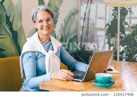 Cheerful senior freelancer woman working from a cozy cafe, embracing freedom and digital lifestyle Cheerful senior freelancer woman working from a cozy cafe, embracing freedom and digital lifestyle 126917406