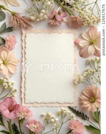 Blank card with scalloped edge surrounded by pastel flowers on white table. 126917678