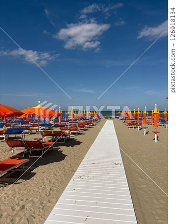 Sandy beach with empty sun loungers and orange umbrellas. Preparing for the beach season. 126918134