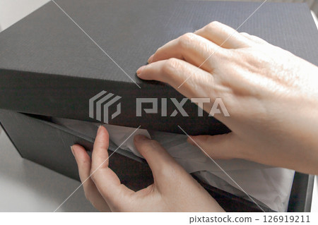 Women's hands unpack a delivered parcel or a gift Women's hands unpack a delivered parcel or a gift 126919211
