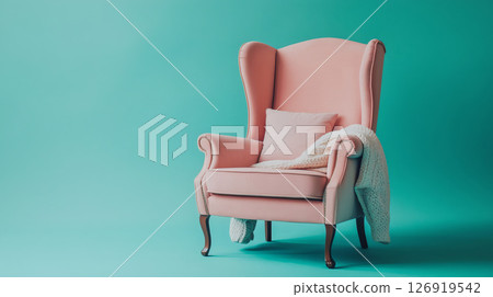 Comfortable pink armchair with blanket and pillow inviting relaxation on turquoise background 126919542