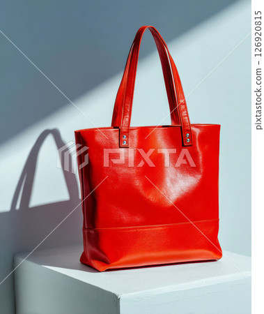 Your It Bag red leather tote with minimal clean lines and soft sheen on shadowed studio surface 126920815
