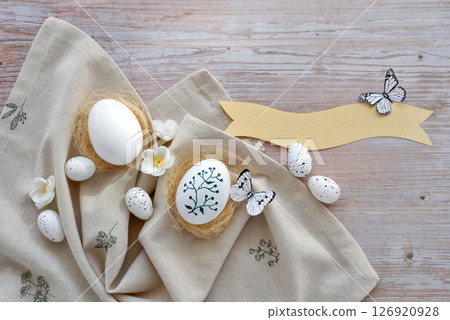 Stylish decorated easter eggs in nests on linen cloth on a light wooden background. Top view.  126920928