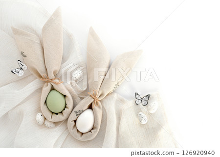 Easter eggs wrapped in a napkins folded like bunny ears on linen cloth. Happy Easter concept. Easter eggs wrapped in a napkins folded like bunny ears on linen cloth. Happy Easter concept. 126920940