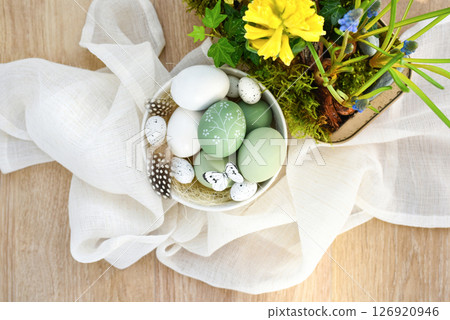 Stylish decorated easter eggs in a white bowl and spring primroses in a pot on linen cloth. Top view 126920946