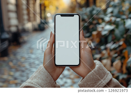 Hands with a smartphone among autumn leaves on the street 126921973