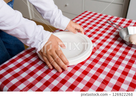 Child setting table with red checkered tablecloth and white plates 126922268