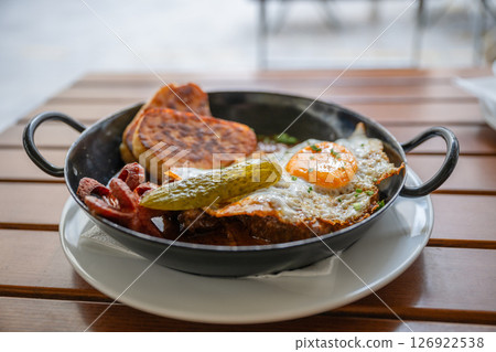 Traditional hearty breakfast with fried egg pickle and sausage in metal skillet outdoors Traditional hearty breakfast with fried egg pickle and sausage in metal skillet outdoors 126922538