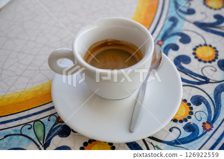 Freshly brewed espresso in white cup on colorful ceramic table outdoors 126922559