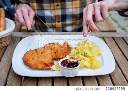 Traditional schnitzel with potatoes and cranberry sauce on white plate outdoors 126922569