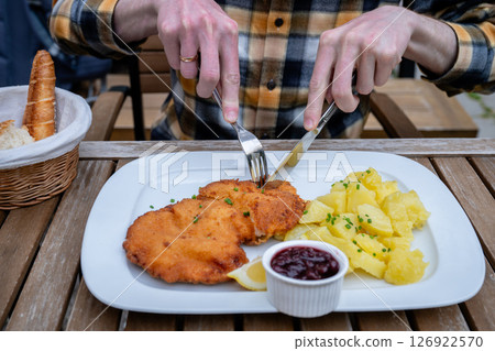 Traditional schnitzel with potatoes and cranberry sauce on white plate outdoors 126922570