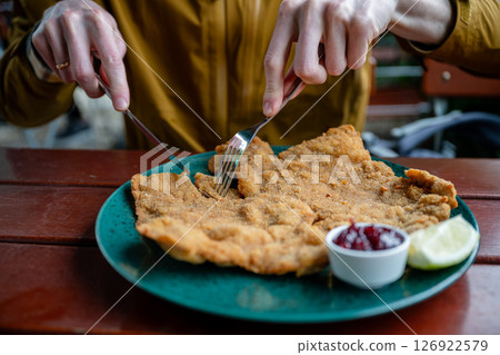Breaded schnitzel with cranberry sauce and lemon slice on a green plate on a wooden outdoor table 126922579