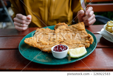 Breaded schnitzel with cranberry sauce and lemon slice on a green plate on a wooden outdoor table 126922583