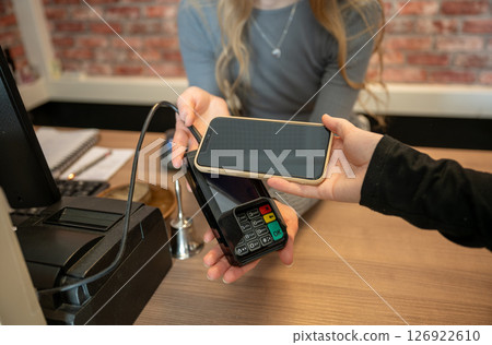 Hand of young woman holding smartphone close to electronic payment machine Hand of young woman holding smartphone close to electronic payment machine 126922610