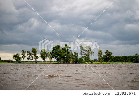 Row of green trees on lake bank with dark storm clouds overhead, concept of moody weather 126922671