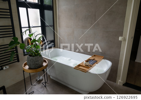 Interior of bathroom with bathtub, dressing table, shelving and large window 126922695