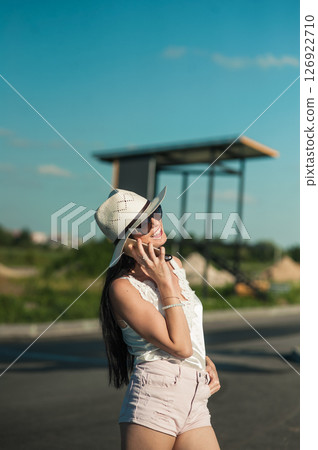 A young woman in a light white outfit is standing in the middle of nature and talking on the phone 126922710
