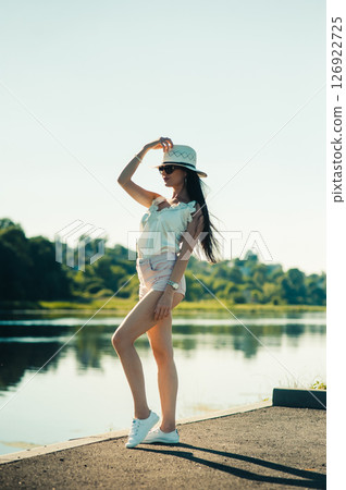 A young lady in white stands by the lake, her back to the water, like a heroine from a movie about summer A young lady in white stands by the lake, her back to the water, like a heroine from a movie about summer 126922725