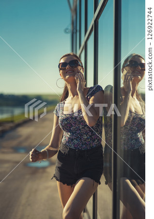 The young lady near the glass surface is engaged in an active phone conversation 126922744