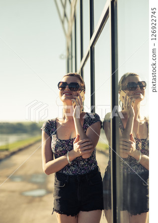 The young lady near the glass surface is engaged in an active phone conversation The young lady near the glass surface is engaged in an active phone conversation 126922745