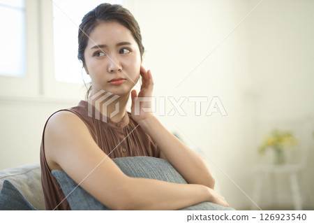 A woman in her 20s who is feeling unwell sitting on a sofa A woman in her 20s who is feeling unwell sitting on a sofa 126923540