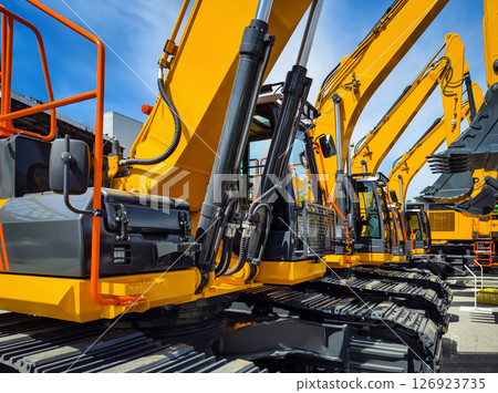 Heavy construction machinery lined up at a construction site under blue sky with minimal clouds 126923735