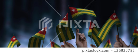 Togo flags in their hands on a blurred urban background Togo flags in their hands on a blurred urban background 126923785