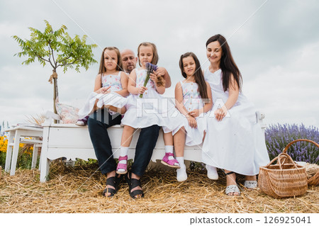 A young father and mother with their three daughters are resting on a retro bench in the lavender field 126925041