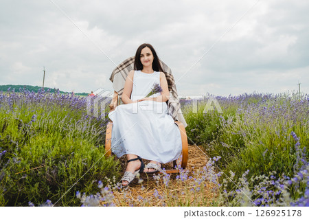 A young woman in a long white dress sits on a rocking chair in the middle of a lavender field A young woman in a long white dress sits on a rocking chair in the middle of a lavender field 126925178