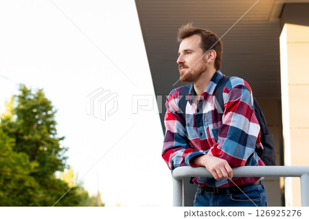Young man leaning on railing looking into distance outdoors 126925276