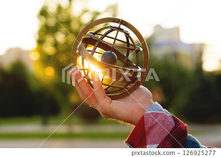 Person holding vintage armillary sphere illuminated by sunset rays Person holding vintage armillary sphere illuminated by sunset rays 126925277