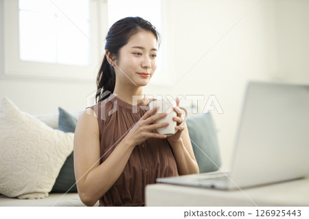 一位二十多歲的女士在客廳裡用筆記型電腦工作 126925443