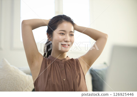 A woman in her 20s stretching while looking at a laptop in the living room 126925446