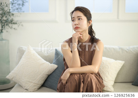 A woman in her 20s who is feeling unwell sitting on a sofa 126925636