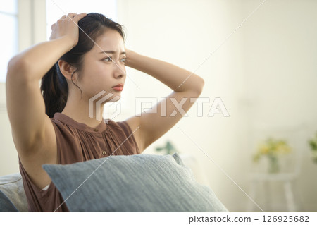A woman in her 20s with a troubled face sitting on a sofa A woman in her 20s with a troubled face sitting on a sofa 126925682