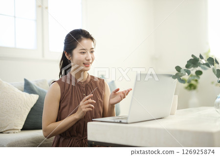 一位二十多歲的女士在客廳裡用筆記型電腦工作 一位二十多歲的女士在客廳裡用筆記型電腦工作 126925874