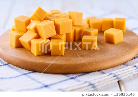 cutting board with cheddar cheese cubes on white kitchen table, selective focus. 126926146