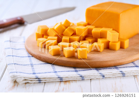 cutting board with cheddar cheese cubes on white kitchen table, selective focus. cutting board with cheddar cheese cubes on white kitchen table, selective focus. 126926151